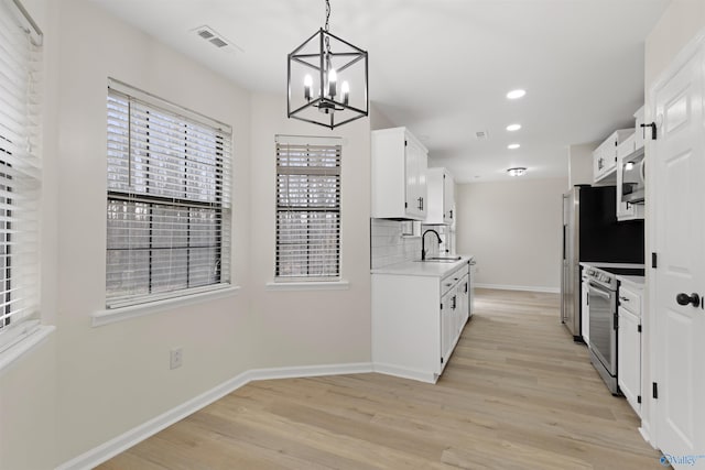 kitchen with appliances with stainless steel finishes, sink, backsplash, white cabinetry, and hanging light fixtures