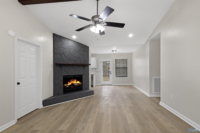 unfurnished living room featuring ceiling fan, lofted ceiling, a stone fireplace, and light hardwood / wood-style flooring