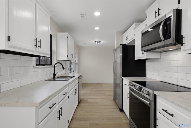 kitchen featuring sink, white cabinetry, light hardwood / wood-style floors, stainless steel appliances, and light stone countertops