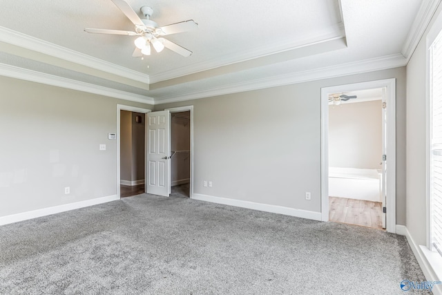 unfurnished bedroom with crown molding, a walk in closet, carpet flooring, and a raised ceiling