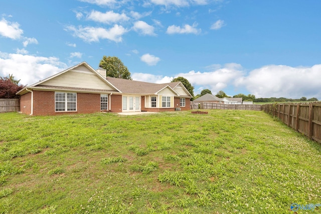 back of house with a chimney, brick siding, a lawn, and a fenced backyard