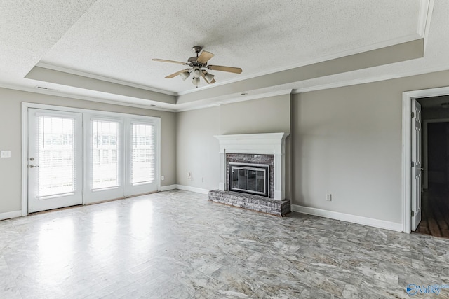 unfurnished living room featuring ceiling fan, a fireplace, a tray ceiling, and tile patterned floors