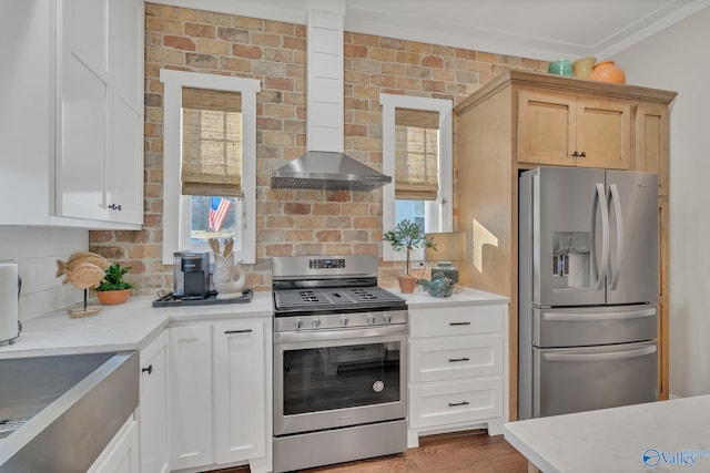 kitchen with brick wall, appliances with stainless steel finishes, light brown cabinetry, and wood-type flooring