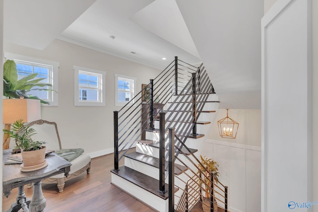 staircase with wood-type flooring, ornamental molding, a wealth of natural light, and a chandelier