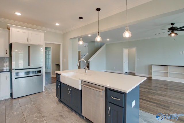 kitchen featuring ceiling fan, stainless steel appliances, an island with sink, decorative light fixtures, and white cabinets