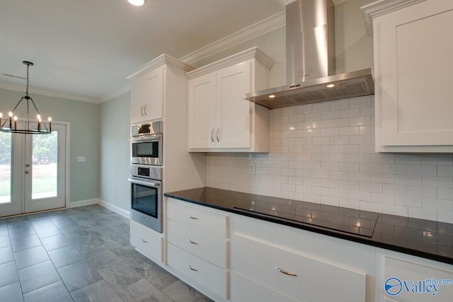 kitchen with wall chimney range hood, hanging light fixtures, tasteful backsplash, cooktop, and white cabinetry