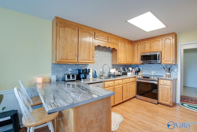 kitchen with sink, kitchen peninsula, appliances with stainless steel finishes, light hardwood / wood-style flooring, and decorative backsplash