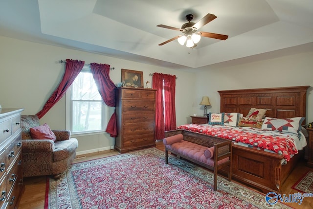 bedroom with light hardwood / wood-style floors, ceiling fan, and a tray ceiling