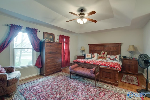 bedroom featuring light hardwood / wood-style floors, ceiling fan, and a tray ceiling