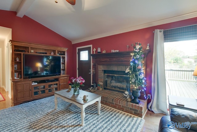 living room featuring lofted ceiling with beams, wood-type flooring, ornamental molding, a brick fireplace, and ceiling fan