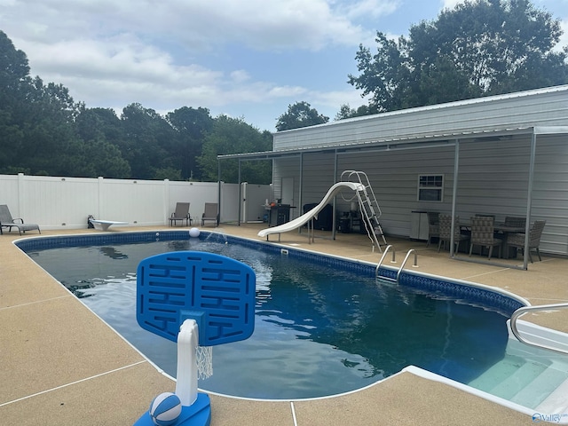 view of swimming pool with a water slide, a diving board, and a patio area