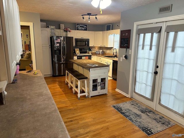 kitchen featuring stove, black dishwasher, stainless steel refrigerator with ice dispenser, white cabinets, and light wood-type flooring