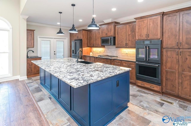 kitchen with appliances with stainless steel finishes, a center island with sink, sink, a healthy amount of sunlight, and backsplash