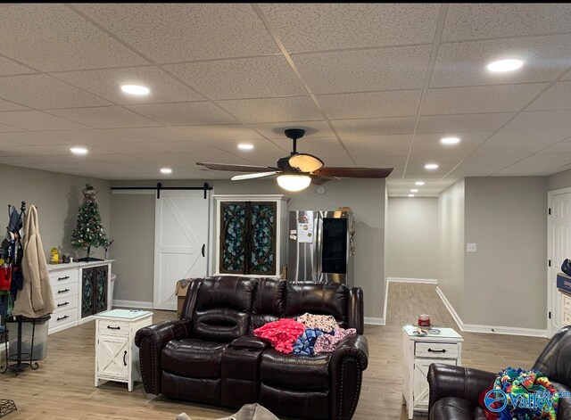 living room featuring light hardwood / wood-style floors, a drop ceiling, a barn door, and ceiling fan