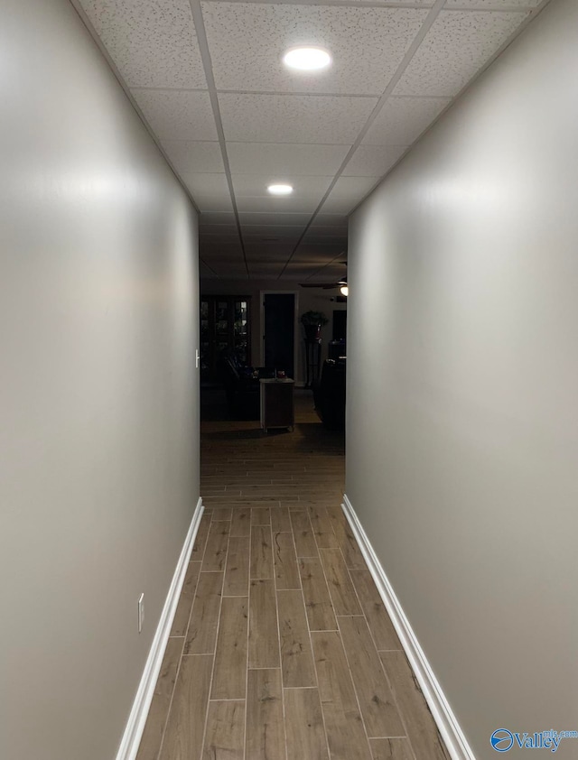 hall with wood-type flooring and a drop ceiling