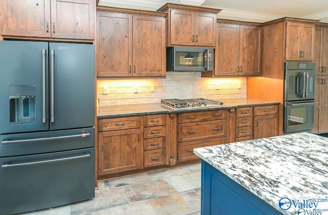 kitchen with appliances with stainless steel finishes, tasteful backsplash, crown molding, light tile patterned flooring, and dark stone countertops