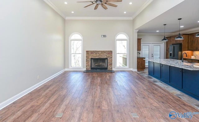 unfurnished living room featuring ceiling fan, hardwood / wood-style floors, ornamental molding, sink, and a stone fireplace