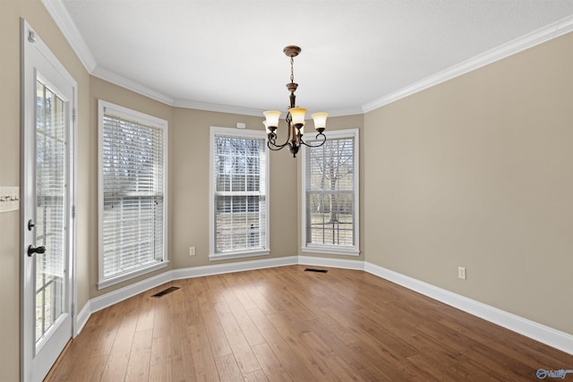 unfurnished dining area with crown molding, wood-type flooring, an inviting chandelier, and baseboards