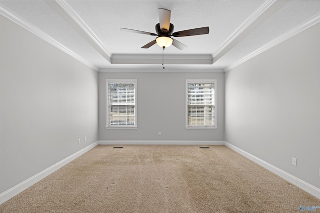 carpeted empty room with a tray ceiling, crown molding, and baseboards