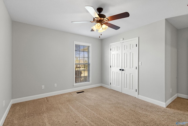 empty room featuring a ceiling fan, carpet flooring, visible vents, and baseboards