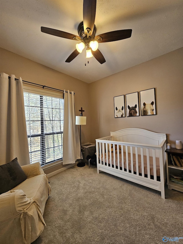 bedroom featuring a ceiling fan, carpet flooring, a crib, and a textured ceiling