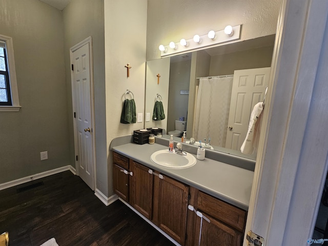 bathroom with visible vents, toilet, vanity, wood finished floors, and baseboards