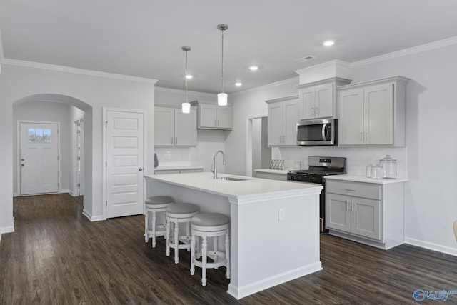 kitchen with sink, hanging light fixtures, appliances with stainless steel finishes, dark hardwood / wood-style flooring, and a kitchen island with sink