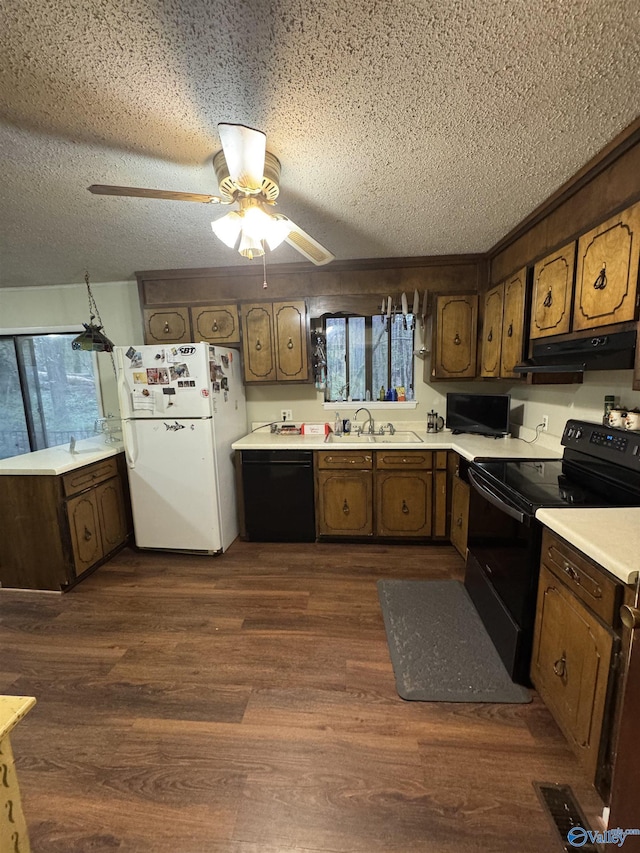 kitchen featuring dark wood-style flooring, light countertops, under cabinet range hood, a sink, and black appliances