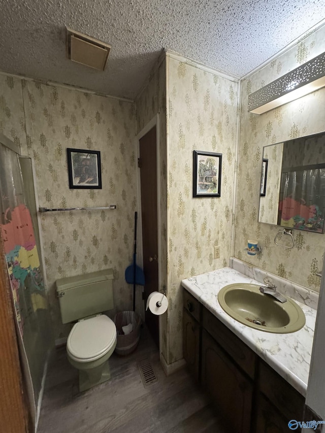 full bath with a textured ceiling, wallpapered walls, vanity, and wood finished floors