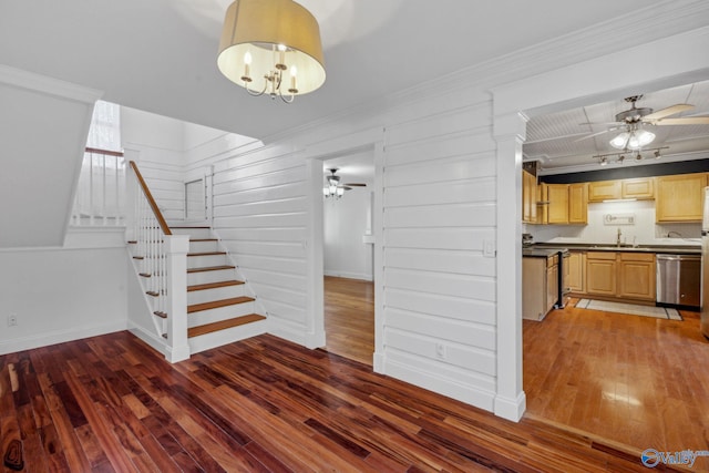 stairs with crown molding, ceiling fan with notable chandelier, and wood-type flooring