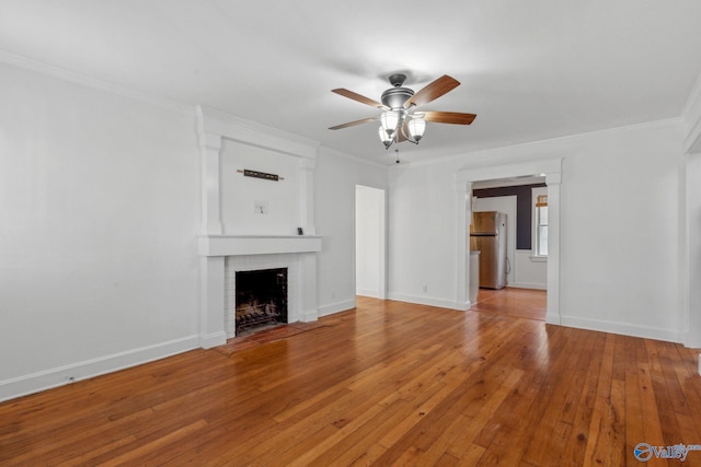 unfurnished living room with light wood-type flooring, a brick fireplace, crown molding, and ceiling fan