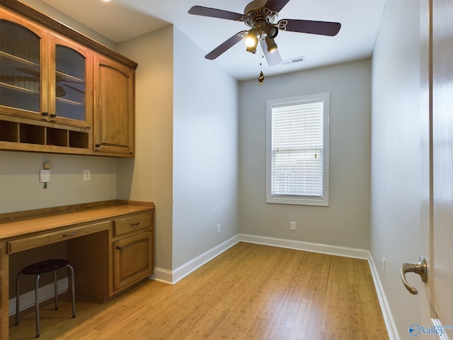 unfurnished office featuring light wood finished floors, built in desk, visible vents, and baseboards