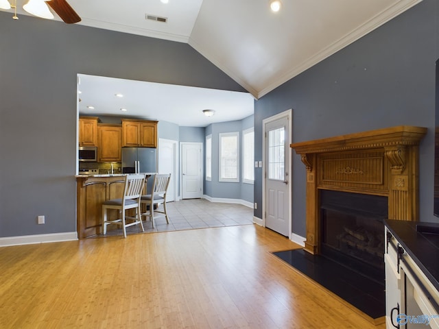 living area featuring light wood finished floors, lofted ceiling, visible vents, ornamental molding, and a fireplace with flush hearth