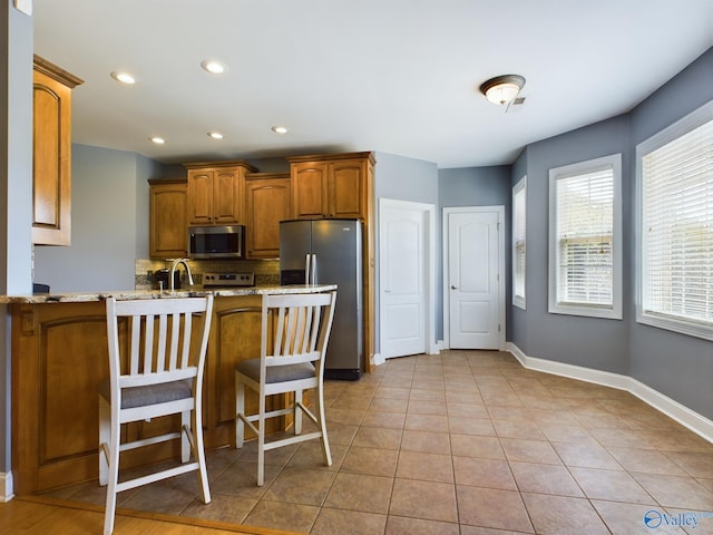 kitchen with light tile patterned floors, a peninsula, baseboards, appliances with stainless steel finishes, and brown cabinetry