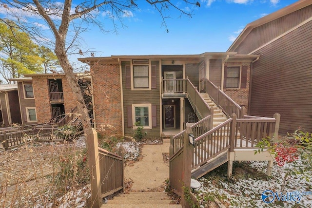 rear view of house with stairs, fence, and brick siding