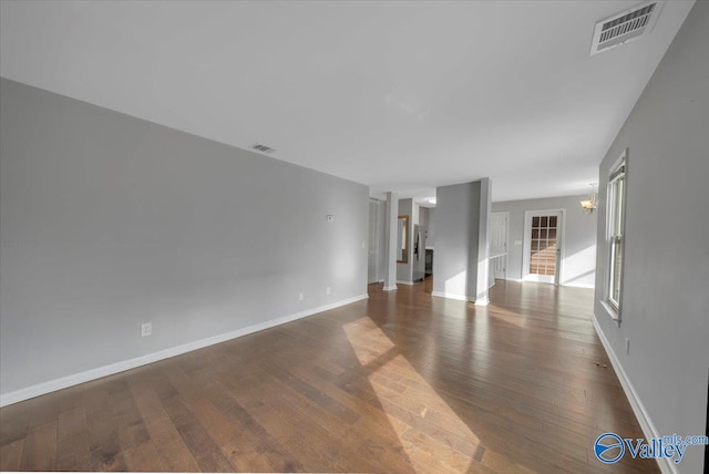 unfurnished living room with baseboards, visible vents, a chandelier, and dark wood-type flooring