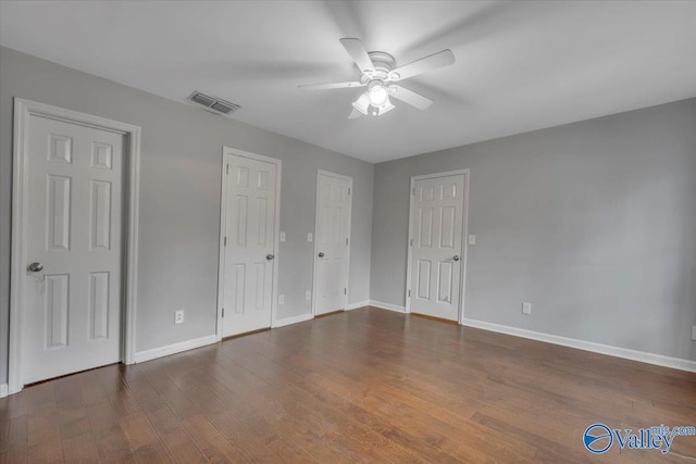 unfurnished bedroom featuring visible vents, two closets, baseboards, and wood finished floors