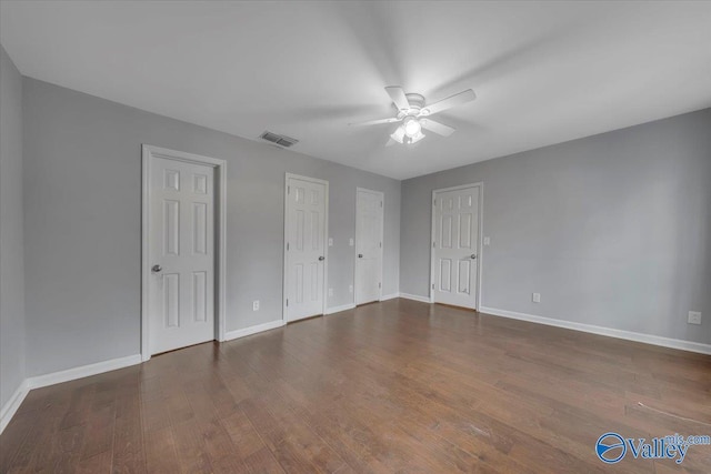 unfurnished bedroom with baseboards, visible vents, ceiling fan, wood finished floors, and multiple closets