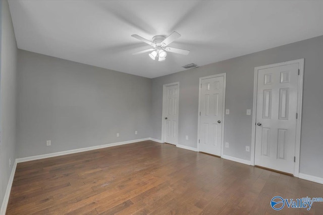 unfurnished bedroom with baseboards, visible vents, ceiling fan, wood finished floors, and multiple closets