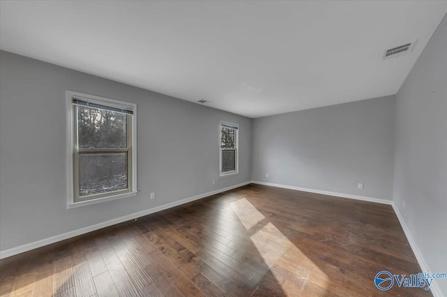 spare room with wood-type flooring, visible vents, and baseboards