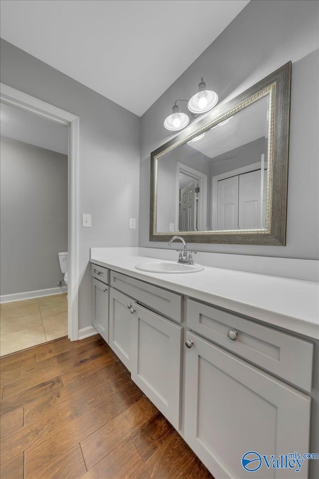 bathroom with toilet, wood finished floors, vanity, and baseboards