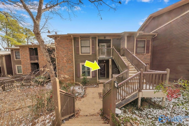 rear view of property featuring stairs, fence, and brick siding