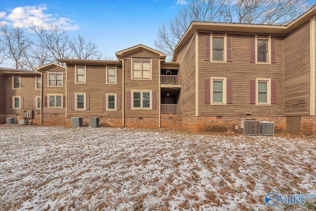 snow covered house with central AC unit, crawl space, and a balcony