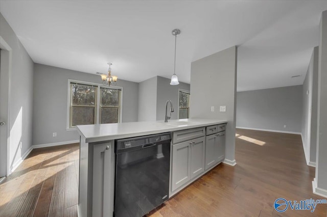 kitchen with black dishwasher, light countertops, wood finished floors, and a sink