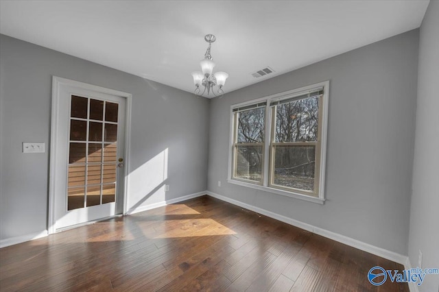 unfurnished room with an inviting chandelier, baseboards, visible vents, and wood finished floors