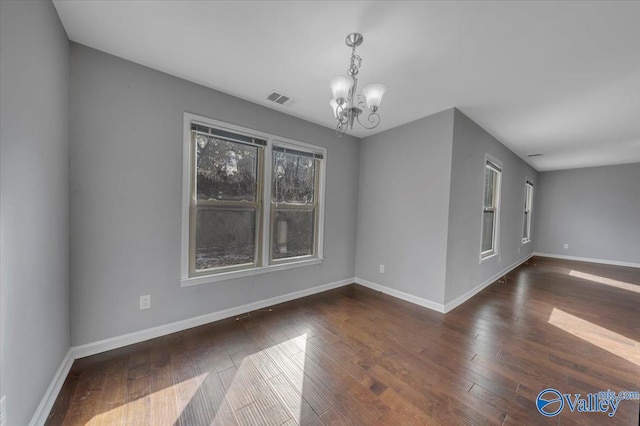 empty room with a chandelier, wood finished floors, visible vents, and baseboards