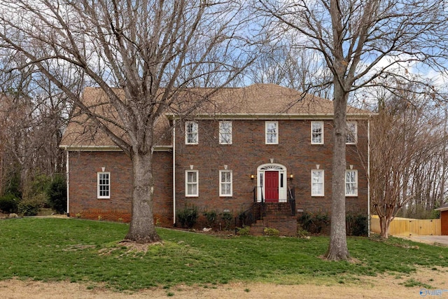 colonial inspired home featuring a front yard, brick siding, and fence