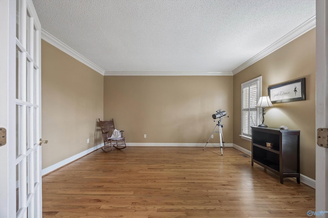 living area with ornamental molding, a textured ceiling, baseboards, and wood finished floors