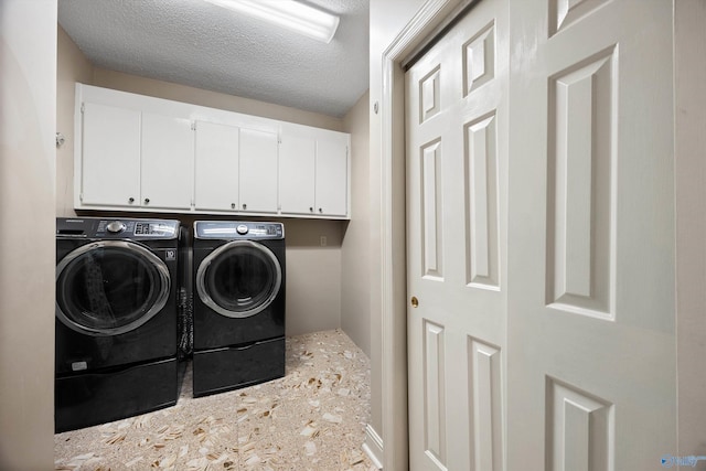 washroom featuring cabinet space, a textured ceiling, and washing machine and clothes dryer