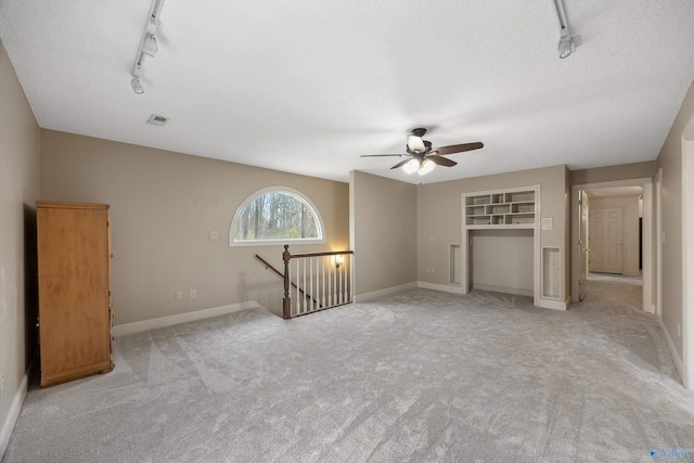 unfurnished living room featuring baseboards, visible vents, light colored carpet, rail lighting, and a textured ceiling